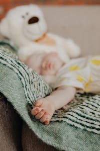 A peaceful sleeping baby with a teddy bear on a green blanket, exuding comfort and warmth.